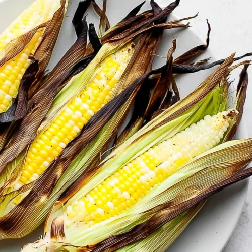 Grilled corn with husks on white plate, charred husks, juicy kernels