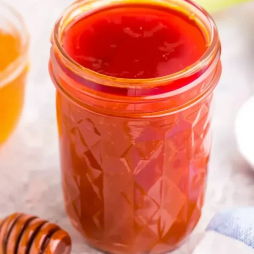 Honey buffalo sauce in a glass jar with honey dipper nearby