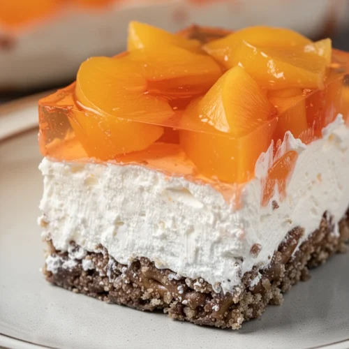 A slice of peach pretzel jello salad with layers of pretzel crust, cream cheese, and peach gelatin.