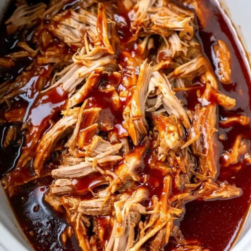 Juicy pulled pork BBQ tenderloin in a slow cooker, coated in glossy barbecue sauce