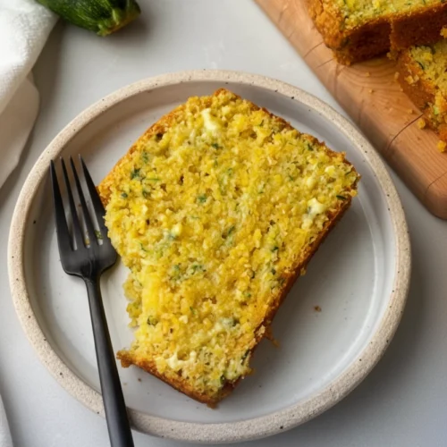 Savory zucchini cornbread loaf slice on plate with fork and fresh zucchini