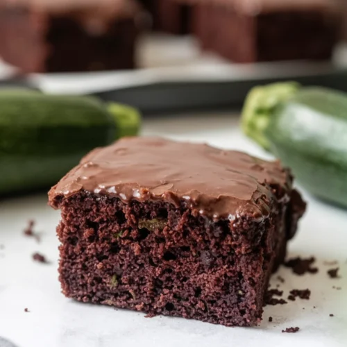 Moist zucchini brownie with chocolate icing, whole zucchinis in background