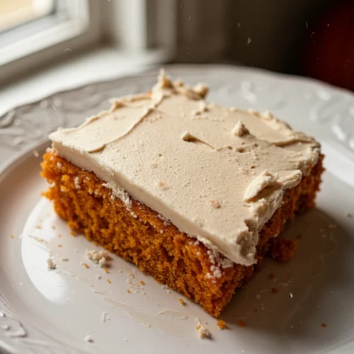 Moist 2 ingredient pumpkin cake slice with white frosting on a white plate