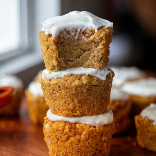 Almond flour pumpkin muffins with cream cheese frosting, stacked on wooden board