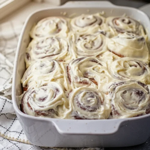 Cinnamon rolls topped with creamy cinnamon roll icing in a white baking dish