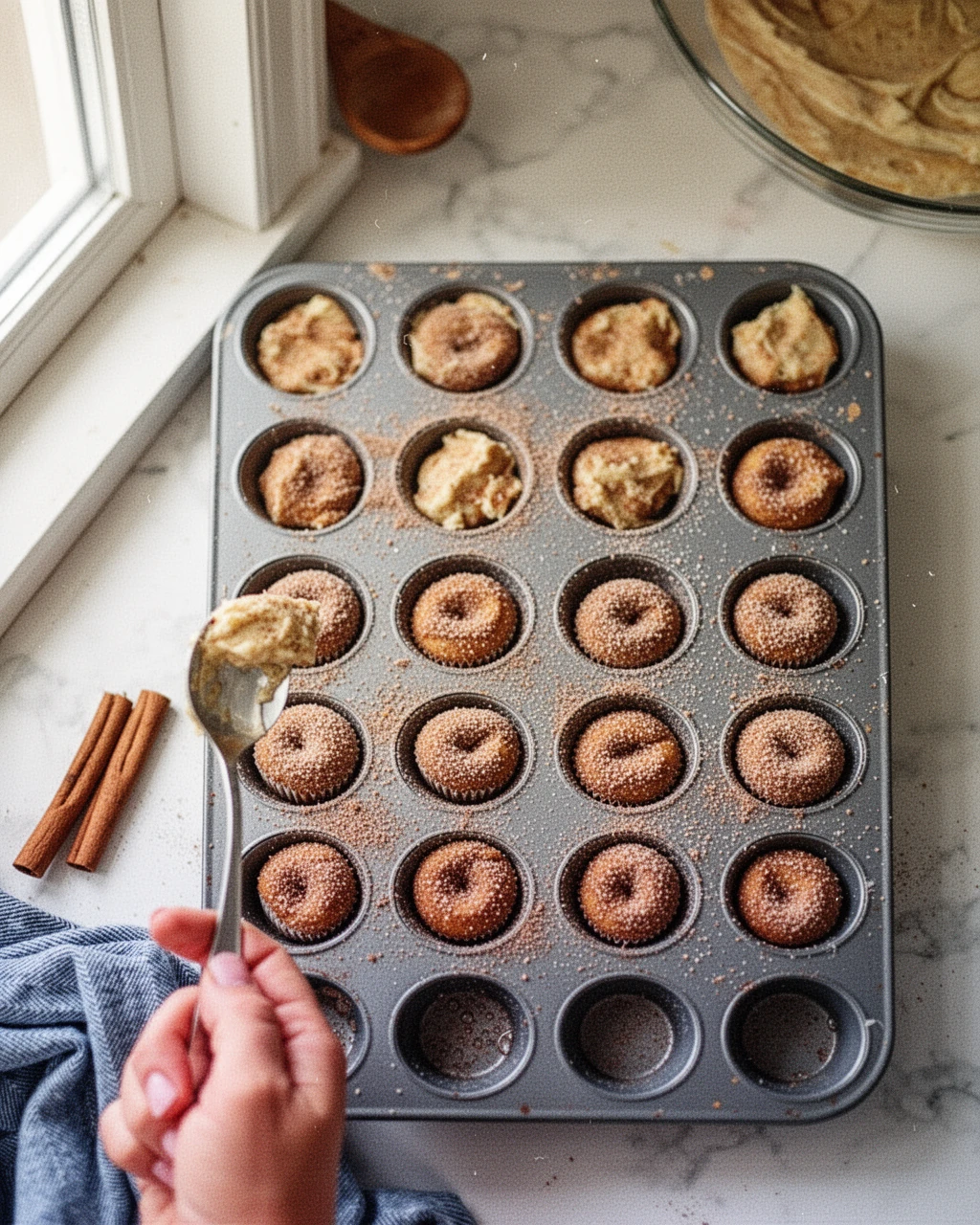 Cinnamon sugar donut muffins batter being spooned into mini muffin tin