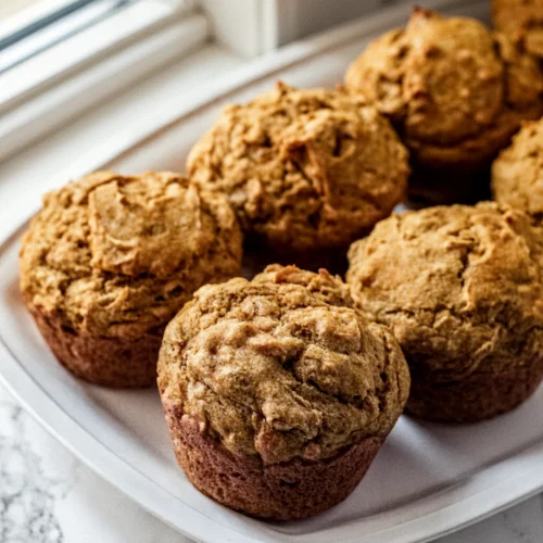 Freshly baked pumpkin banana muffins on a white plate with bananas in background