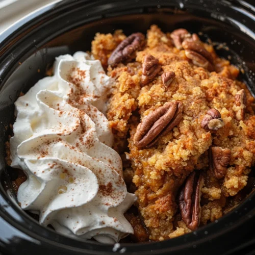 Slow cooker pumpkin cobbler with pecans and whipped cream in a white bowl