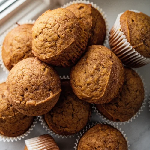Delicious Snickerdoodle Pumpkin Muffins to Savor 1 Golden-brown snickerdoodle pumpkin muffins in white liners on marble