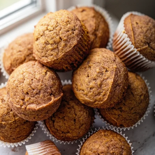 Snickerdoodle pumpkin muffins in white liners on a marble surface